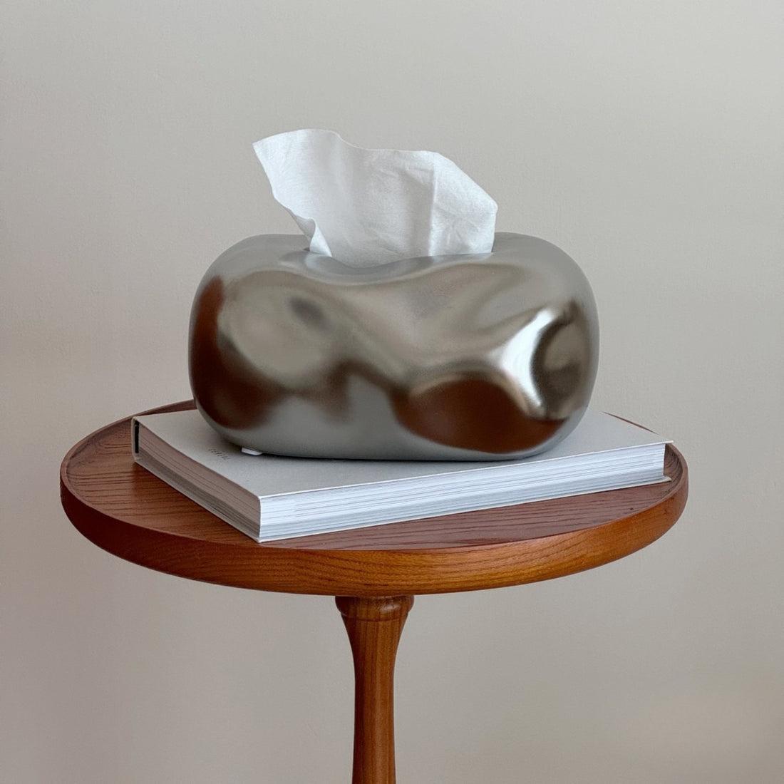 A warmly styled living room coffee table with a tissue cover and book